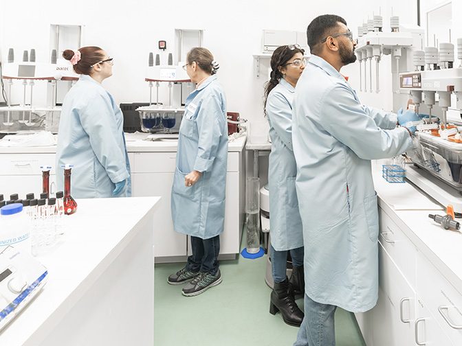 Four scientists in lab coats working at benches in a pharmaceutical laboratory