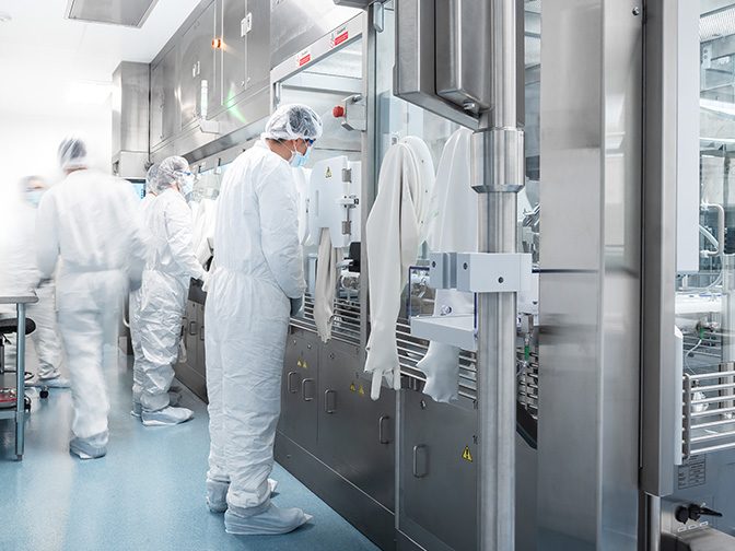 Gowned operators at a stainless-steel aseptic filling line in a cleanroom